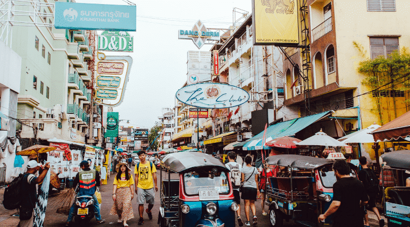 A busy Bangkok street fliled with people, shops, and tuk tuks. 