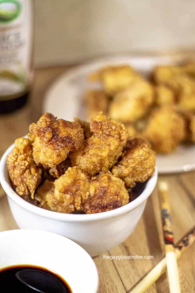 A bowl full of Korean fried chicken next to some Korean fried chicken sauce and chopsticks.