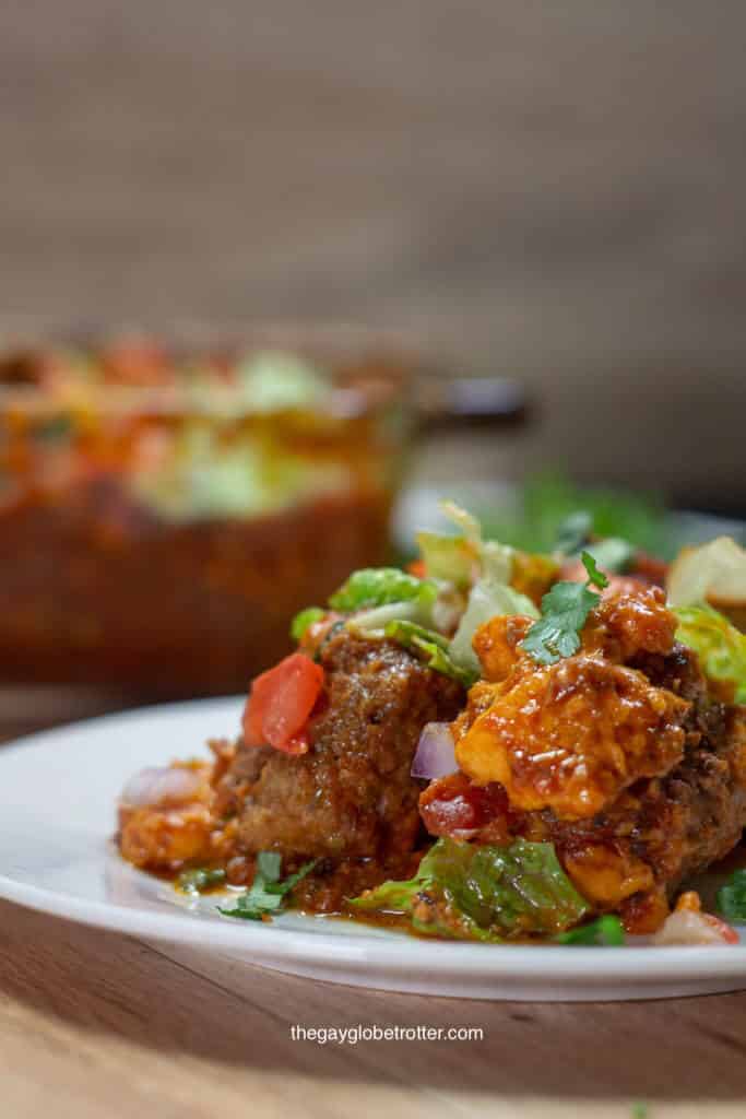 A plate of taco meatball casserole topped with tomatoes, lettuce, and cheese.