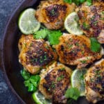 An overhead shot of cilantro lime chicken in a cast iron pan surrounded by fresh limes and cilantro.