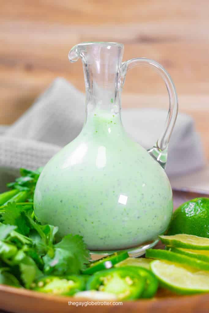 A jar of Peruvian green sauce surrounded by limes, cilantro, and jalapenos.