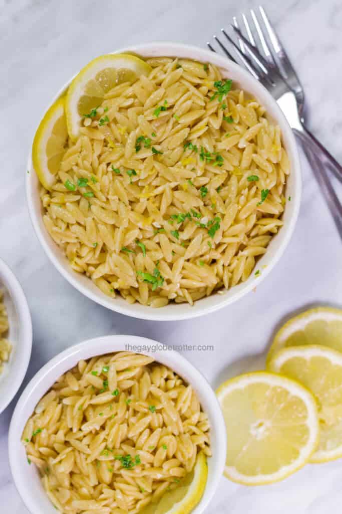 A flat lay photo of lemon parmesan orzo in 2 bowls with some forks.