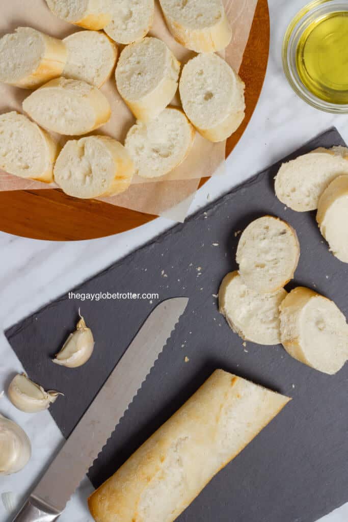 A knife slicing a baguette into crostini pieces.