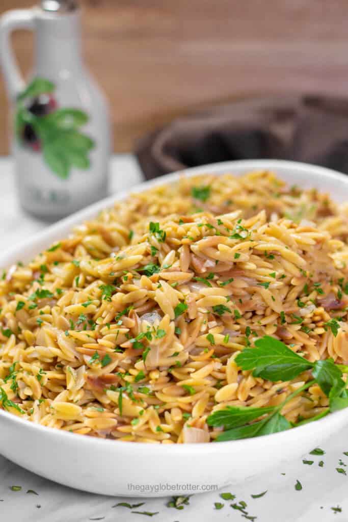A serving platter full of rice pilaf with orzo topped with parsley.