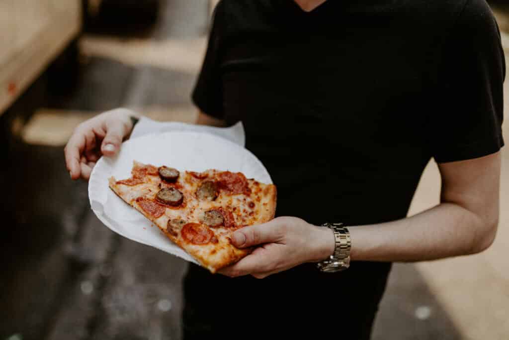 A man holding a plate of pizza on a street.