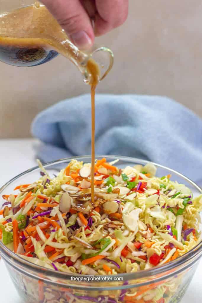 A serving bowl of ramen noodle salad with Asian sesame dressing being poured into it.