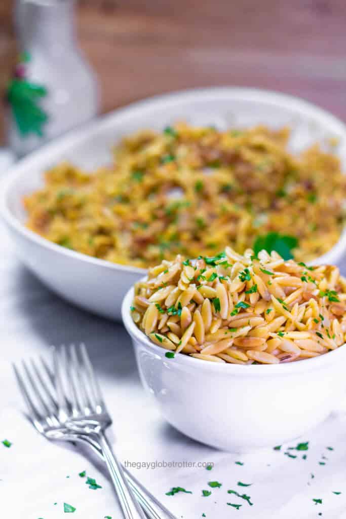 A bowl full of rice pilaf with orzo, with a serving platter of orzo pilaf behind it.