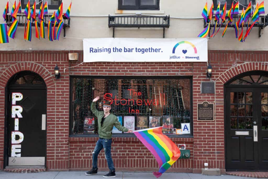 A man waving a rainbow flag in front of The Stonewall Inn.