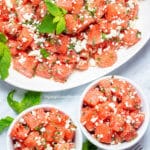A serving platter of watermelon feta salad with two bowls full of salad next to it.