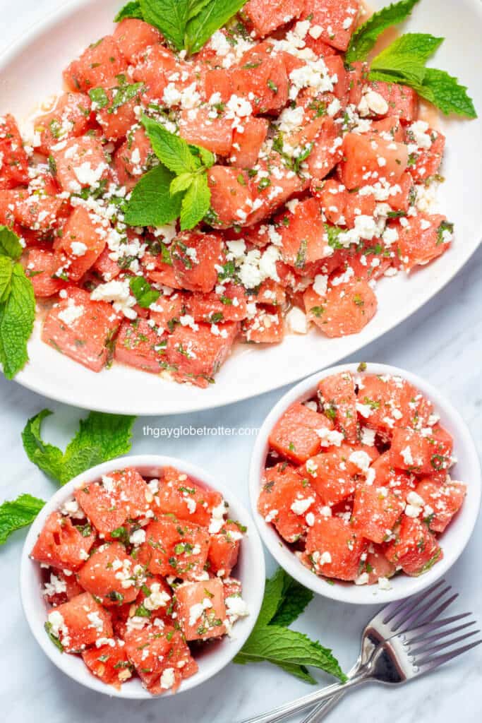 A serving platter of watermelon feta salad with two bowls full of salad next to it.