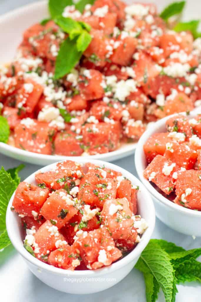 Two bowls of watermelon feta salad with a platter of it behind them.