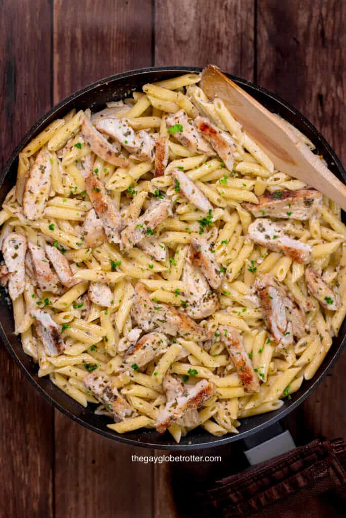 A pot full of creamy chicken pesto pasta with a wooden spoon.