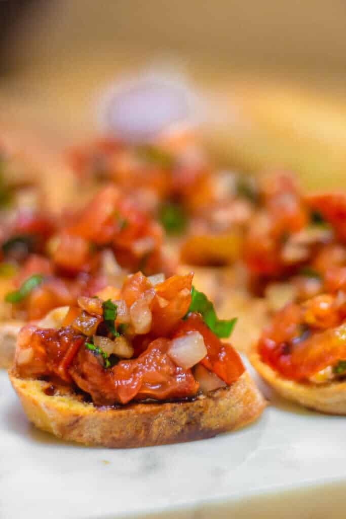 Bruschetta on crostini on a serving board with fresh basil.