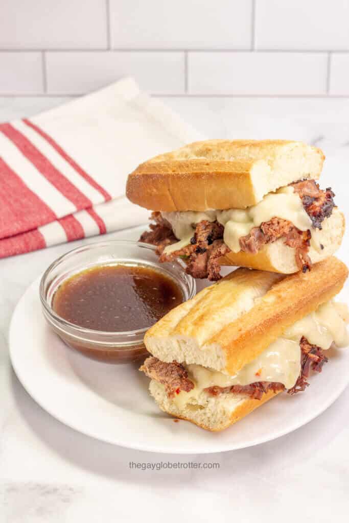 A french dip sandwich piled on a plate next to au jus.