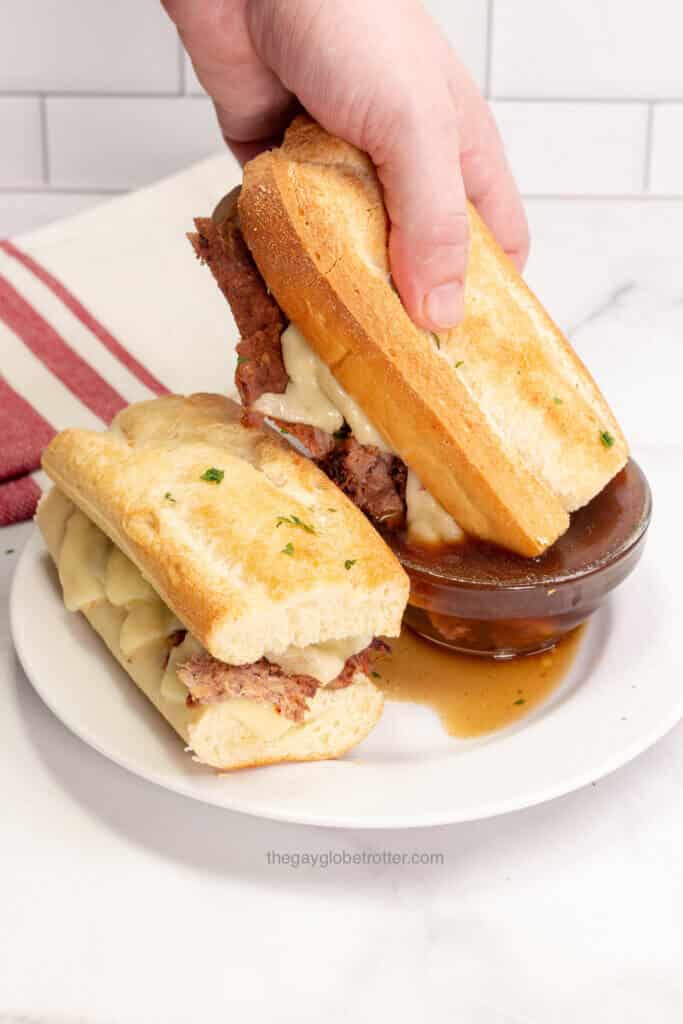 A french dip sandwich being dipped into au jus.