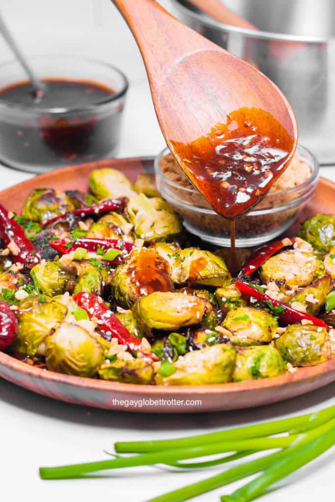 A spoon pouring sauce on kung pao brussels sprouts.