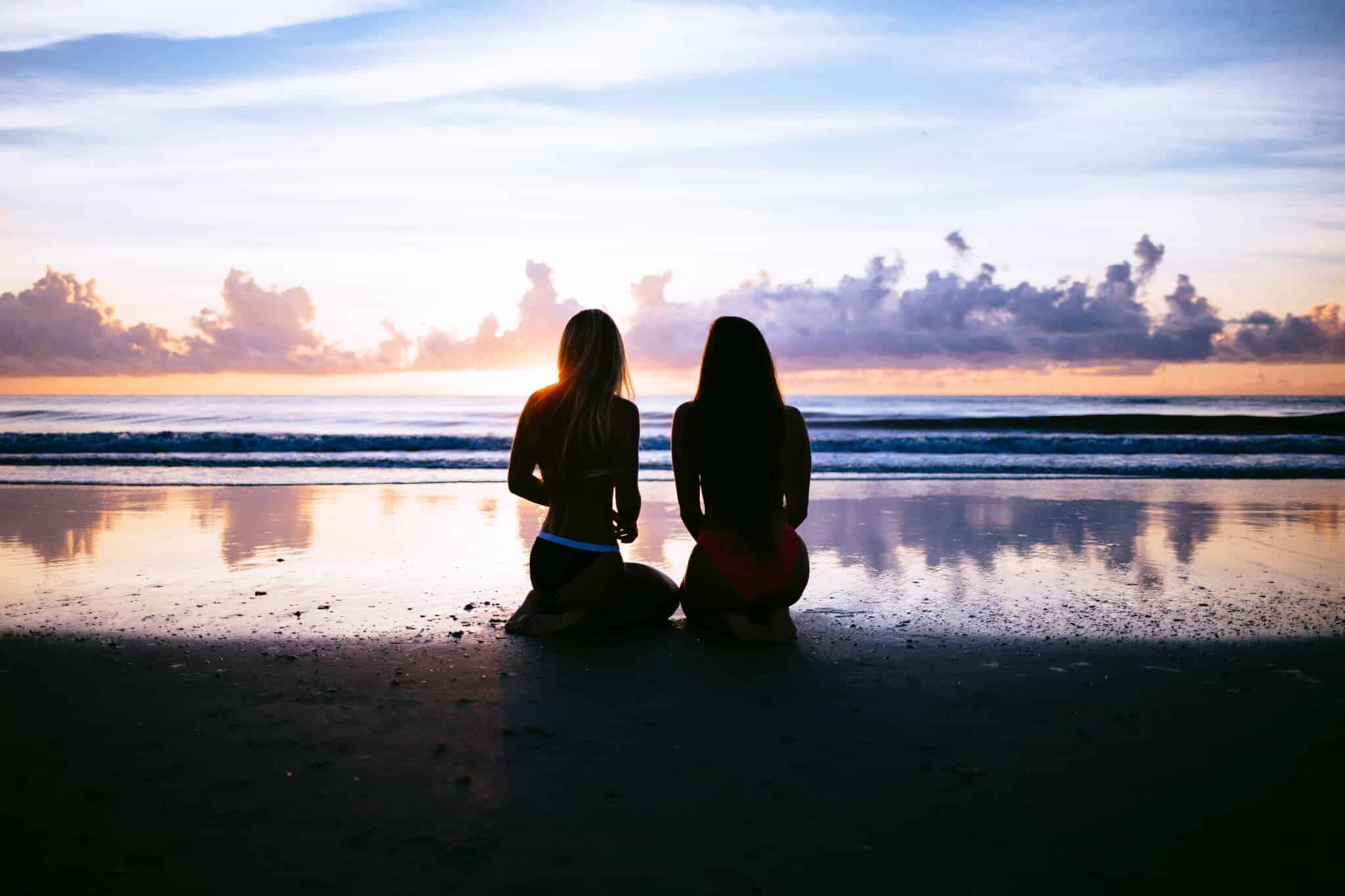 Two silhouetted women sitting on a beach