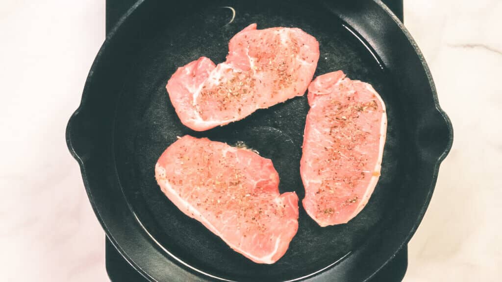 A process shot of pork chops being seared in a cast iron pan.