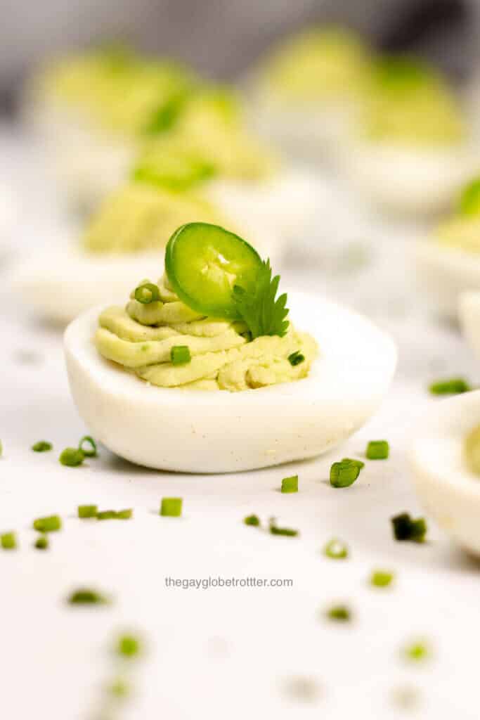 An avocado deviled egg garnished with cilantro, jalapeno, and chives.