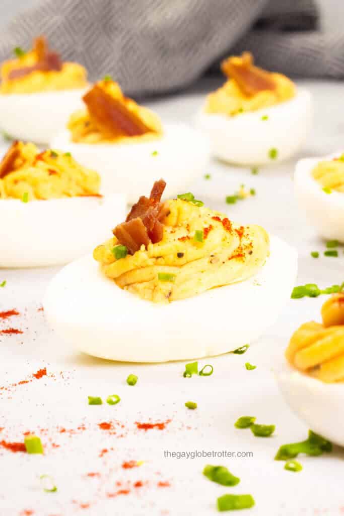 A close up of a bacon deviled egg with chives and paprika.