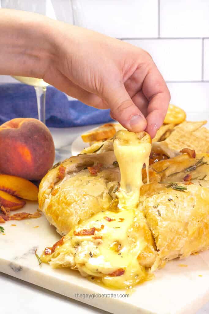 A hand dipping a cracker into baked brie.