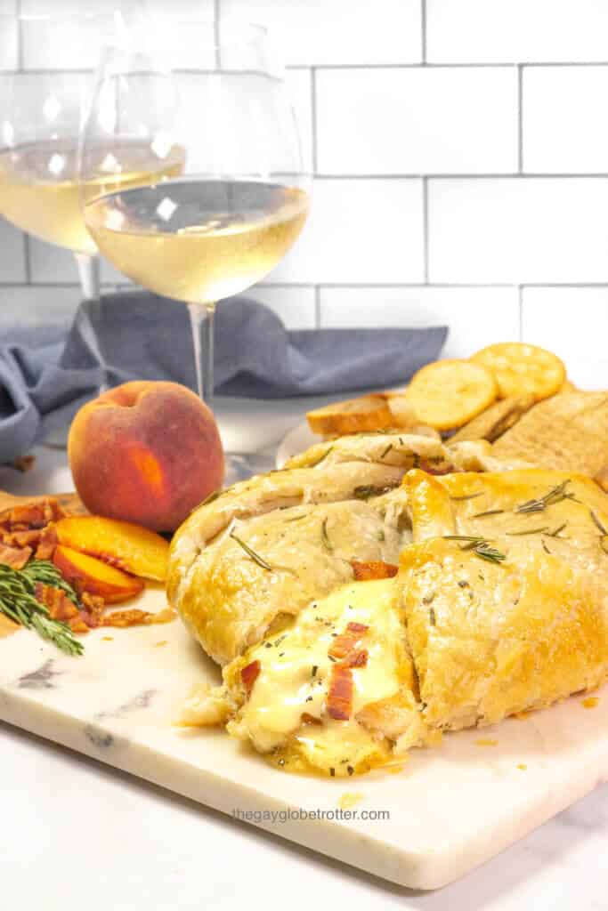 A serving platter with rosemary bacon peach brie en croute sliced open.