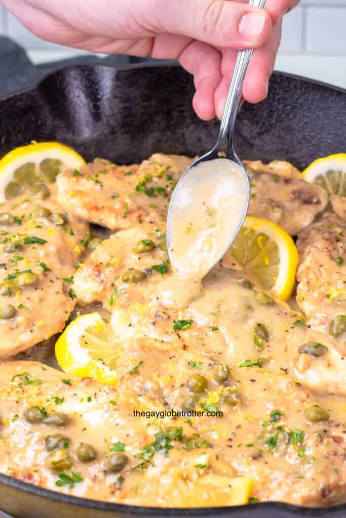 A spoon drizzling lemon sauce over chicken piccata.