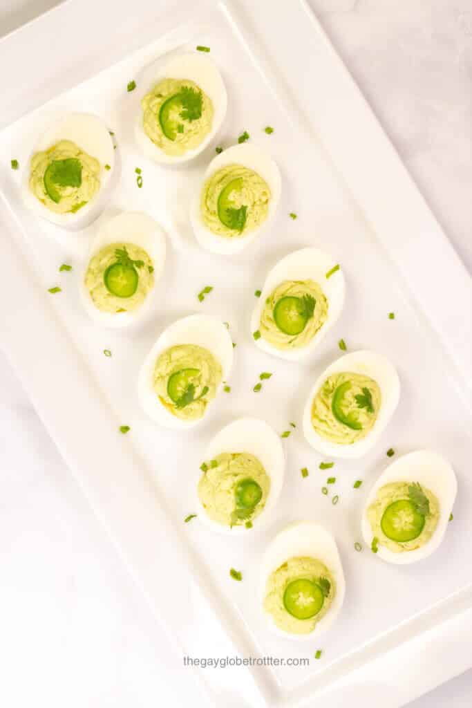 Ten avocado deviled eggs on a white serving plate garnished with chives.