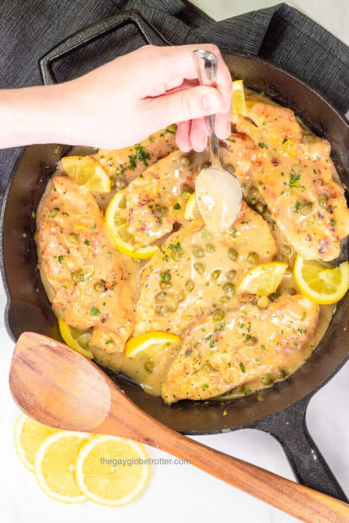 A spoon drizzling sauce over lemon chicken piccata in a pan.