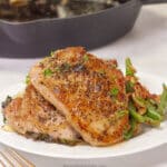 Pan seared pork chops on a plate next to green beans and mashed potatoes.