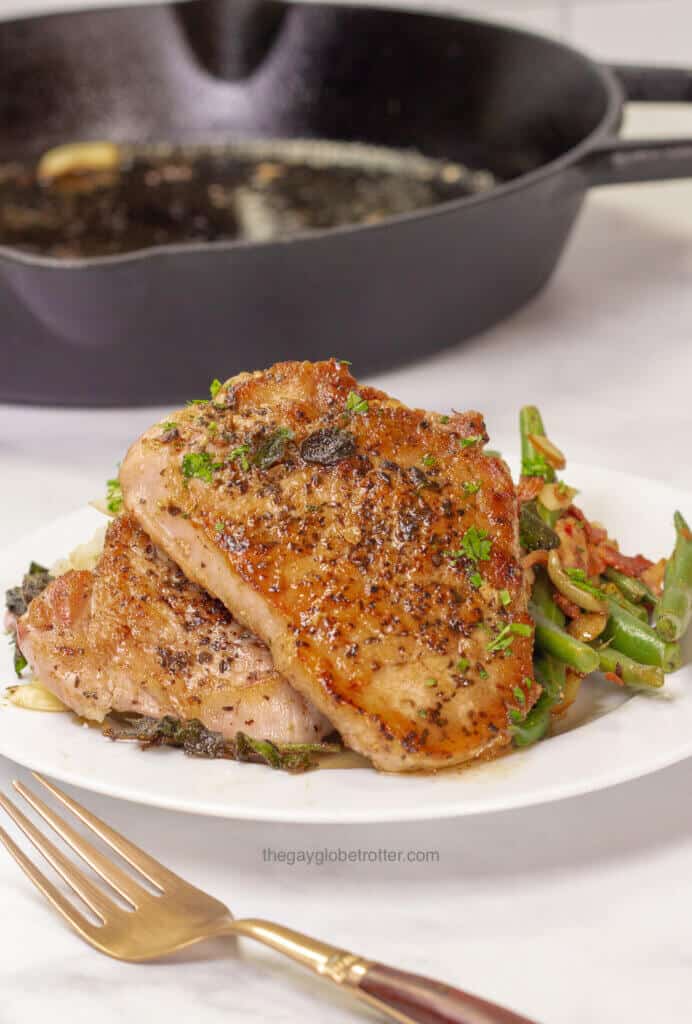 Pan seared pork chops on a plate next to green beans and mashed potatoes.