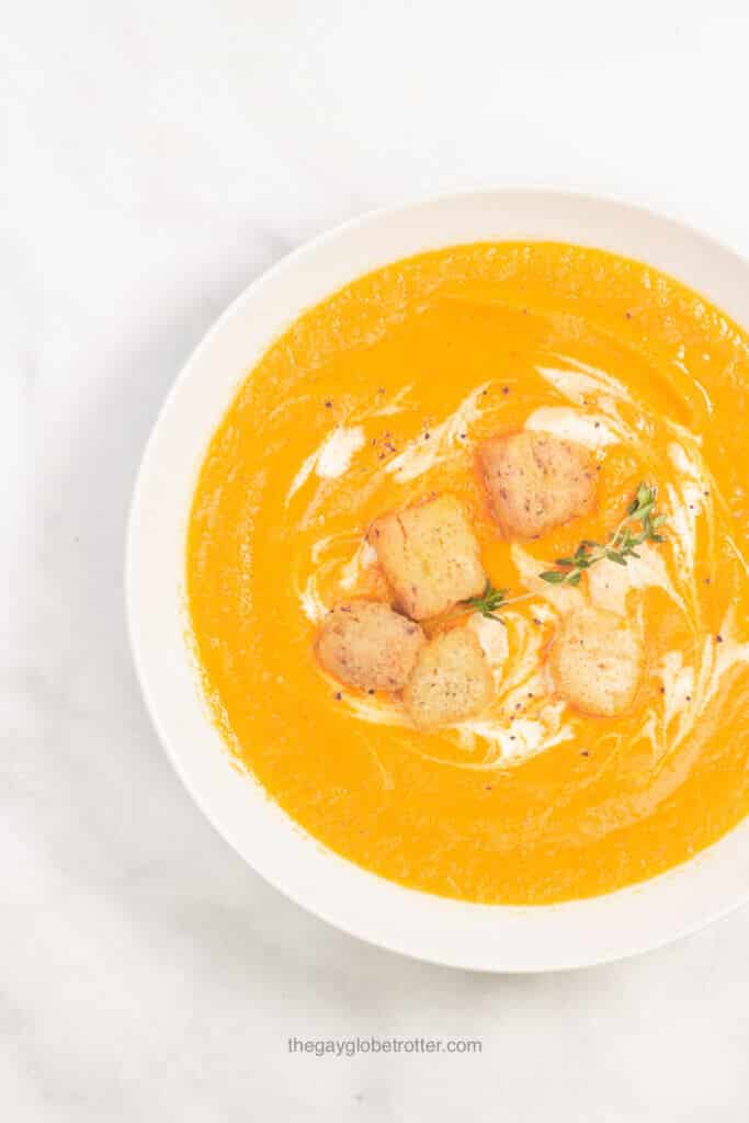 A bowl of carrot ginger soup garnished with croutons and thyme.