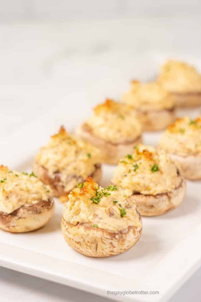 A serving platter full of cream cheese stuffed mushrooms with bread crumb topping and fresh parsley.
