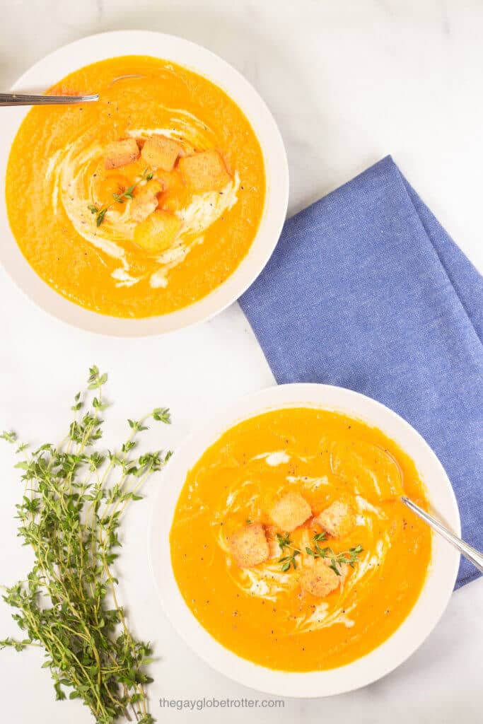 Two bowls of creamy carrot soup next to a bunch of thyme. 