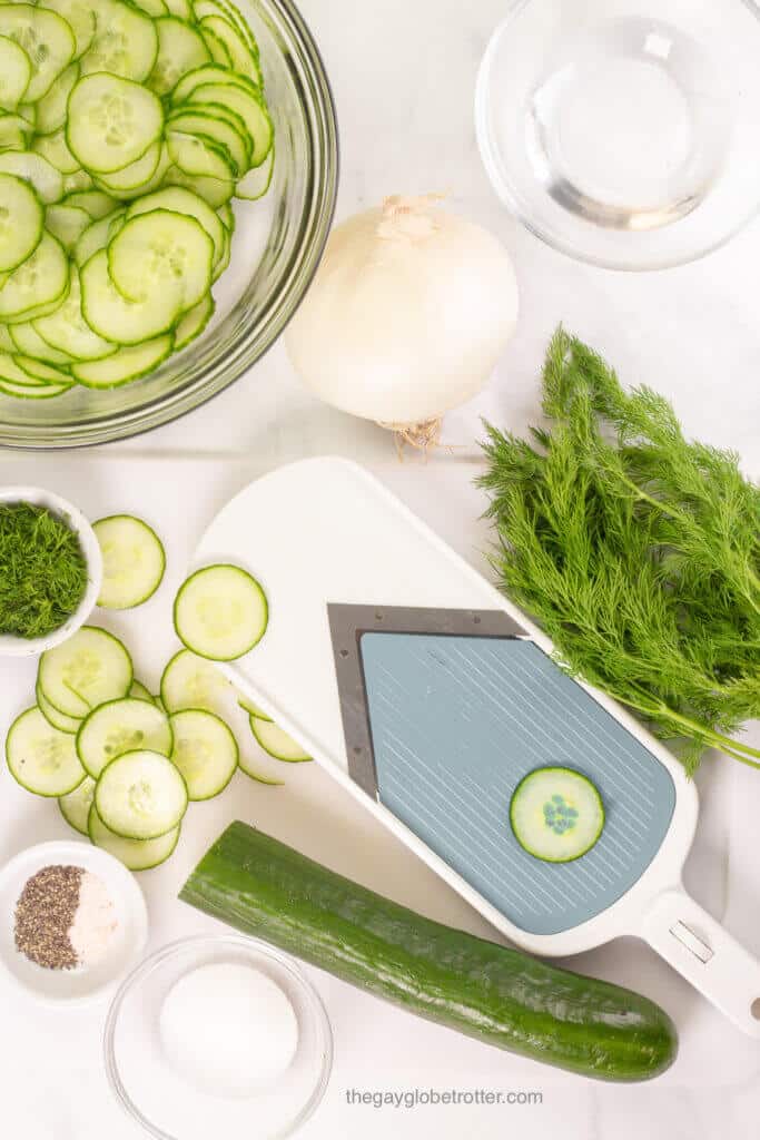 A process shot of a mandolin slicing cucumbers for cucumber salad.