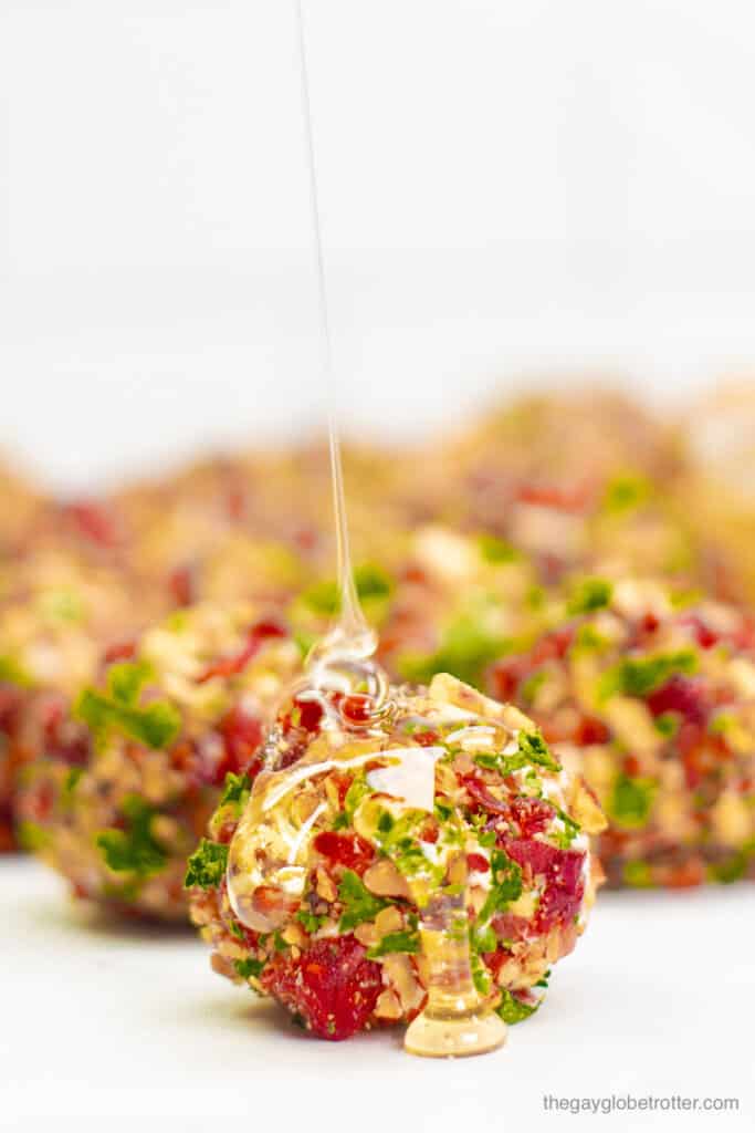 A cranberry pecan cheese ball bite being drizzled with honey.