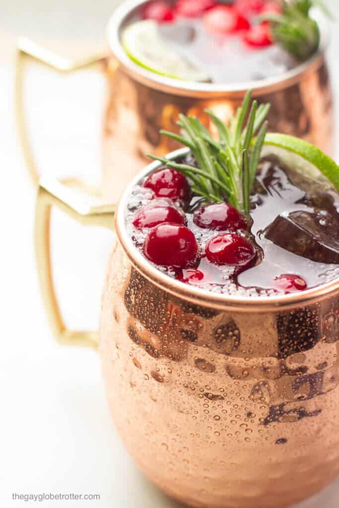 A close up of a cranberry moscow mule garnished with lime, cranberries, and fresh rosemary.