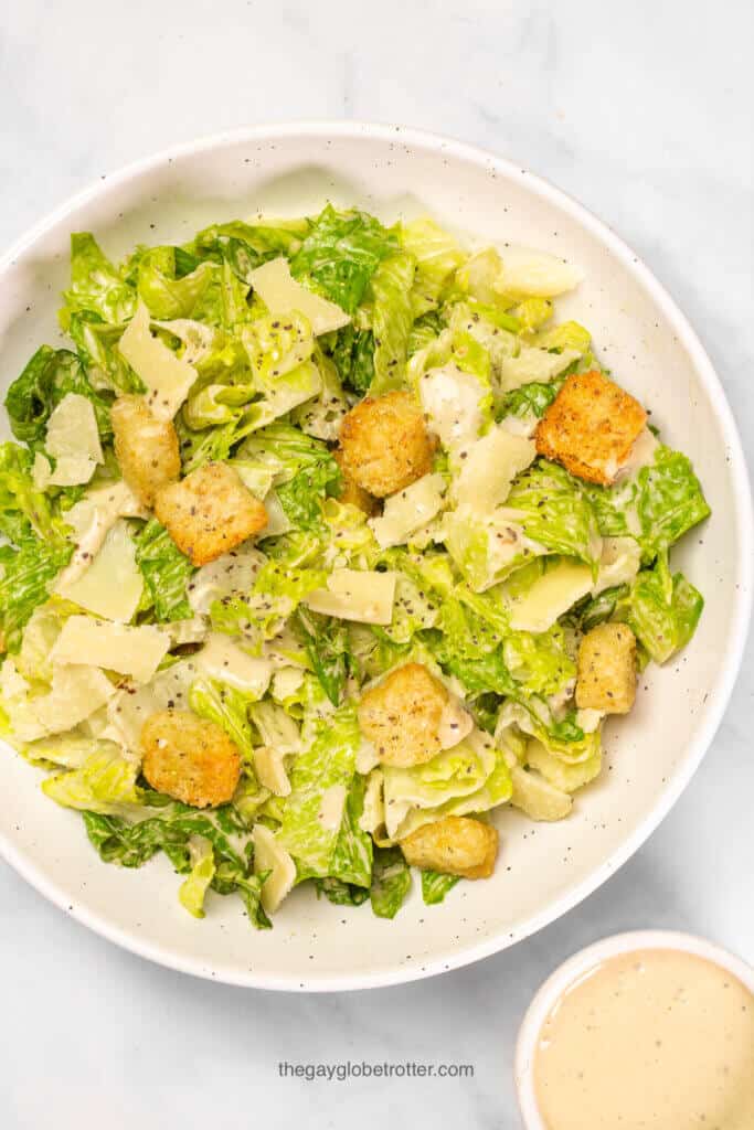 A bowl of classic caesar salad next to caesar salad dressing.