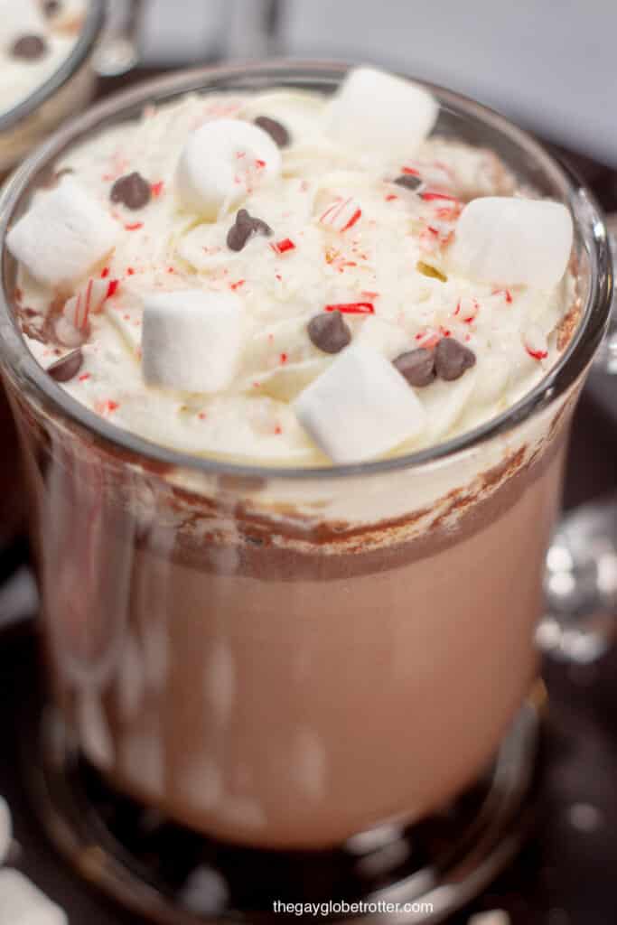 A close up of hot chocolate with candy cane pieces, chocolate chips, marshmallows, and whipped cream.