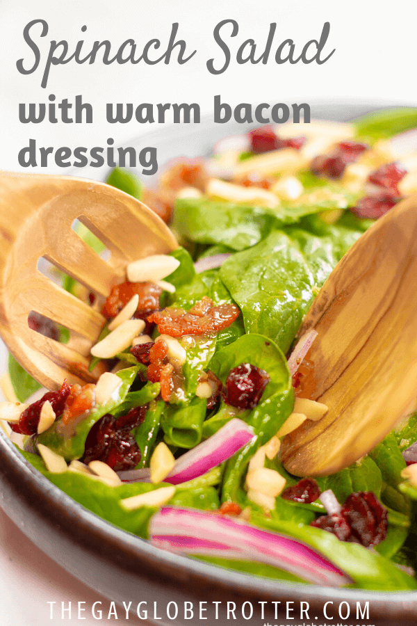 Salad being tossed in a serving dish with warm bacon dressing.