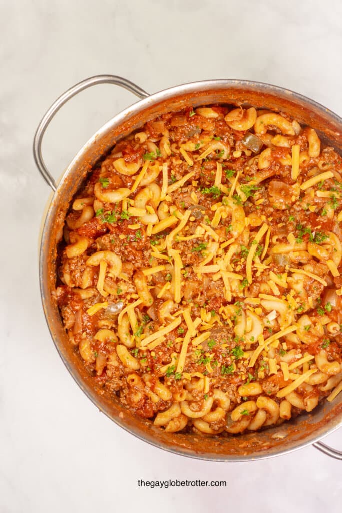 A stock pot of american goulash topped with cheese.