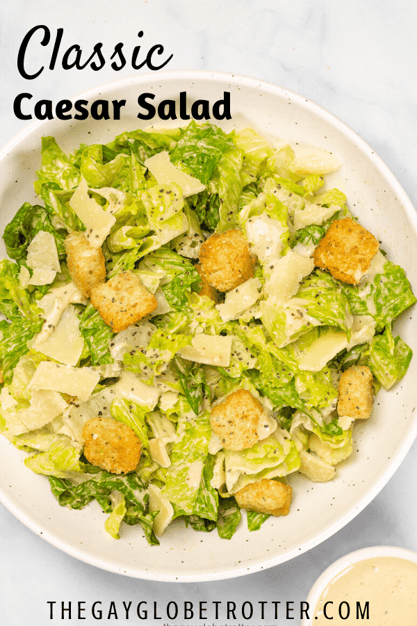 A big serving bowl of classic caesar salad next to caesar salad dressing.