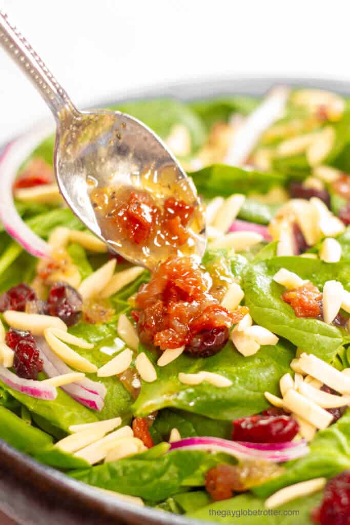 Hot bacon dressing being spooned over a spinach salad.