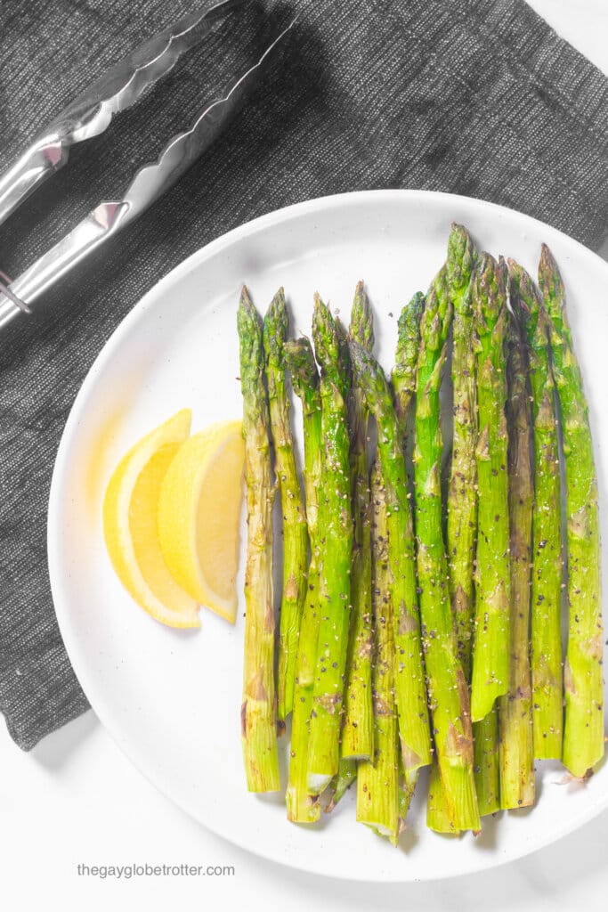 Air fryer asparagus on a plate with two lemon wedges.