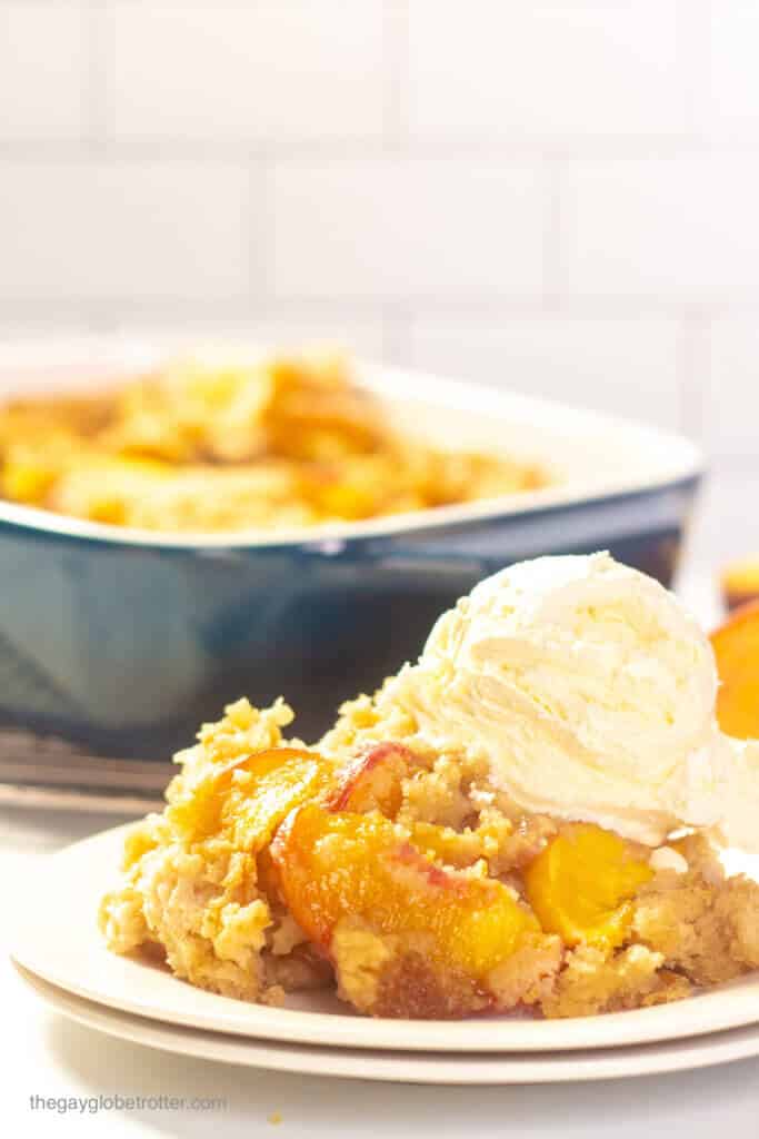 A serving of Bisquick peach cobbler on a plate with a scoop of vanilla ice cream.