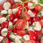 Olive oil being drizzled on cherry tomato caprese salad.