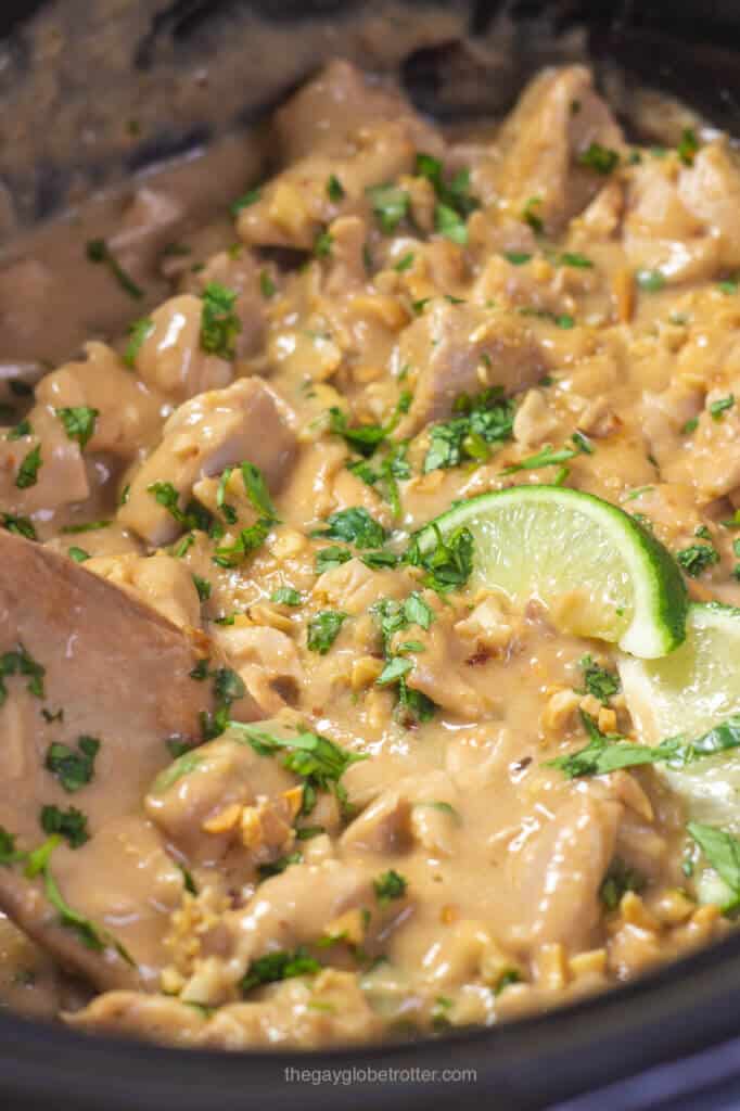 A spoon scooping slow cooker thai peanut chicken with limes and cilantro.