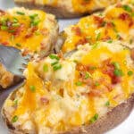 A fork picking up some of a twice baked potato topped with cheese and chives.