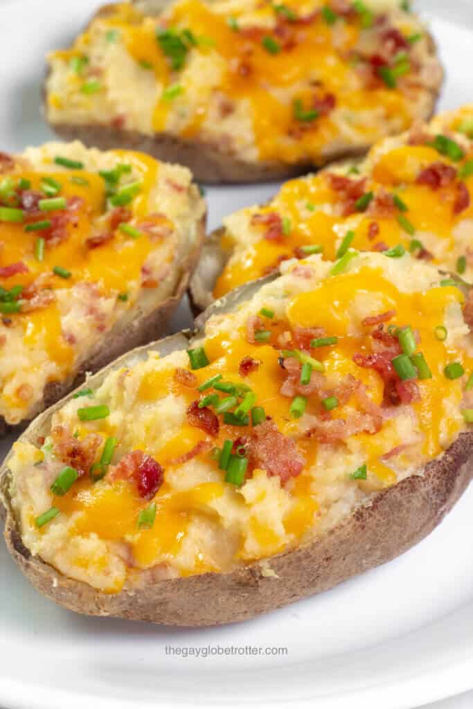 A twice baked potato on a serving platter with chives and bacon.