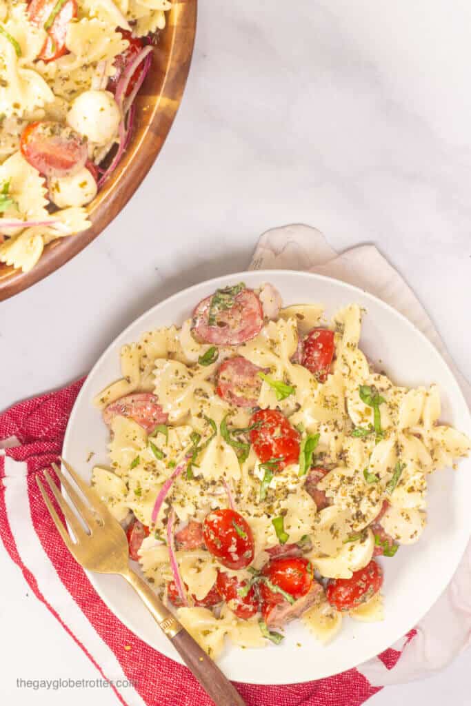 A plate of caprese pesto pasta salad with a gold fork and basil garnish.